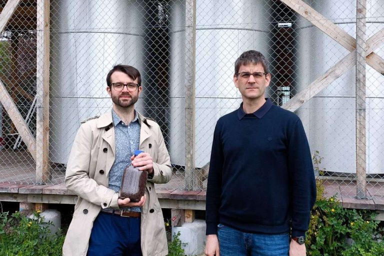 ETH-Forschenden Samuel Heiniger (links, mit einem Glas Eisenerz) und Professor Wendelin Stark vor den drei Eisenreaktoren am Campus Hönggerberg der ETH Zürich