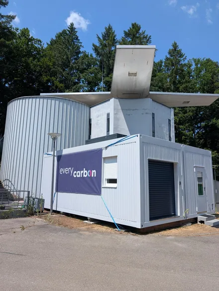 everycarbon-pilotanlage-container-440 Weißer Anlagencontainer mit EveryCarbon-Banner neben einem Betriebsgebäude