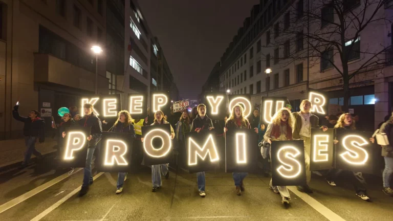 Junge Menschen tragen bei einer nächtlichen Demonstration in Berlin leuchtende Buchstaben mit der Aufschrift Keep your promises
