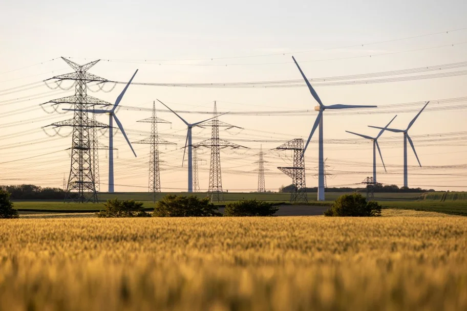 Höchstspannungsmasten und Windräder hinter einem Getreidefeld im Abendlicht