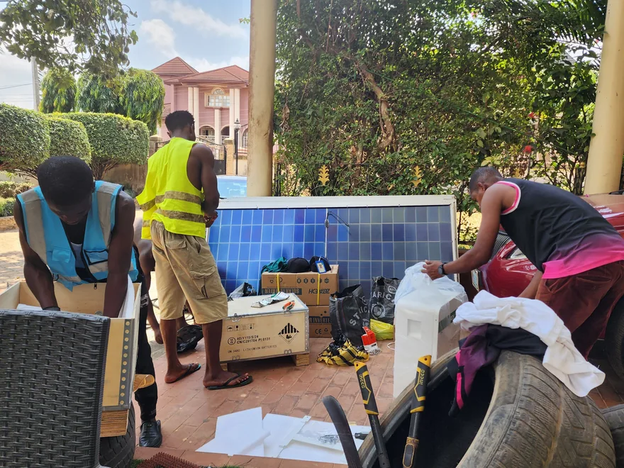 Solarmodule lehnen vor einem Wohnhaus in Onitsha, Nigeria, zwei Installateure packen daneben Geräte aus