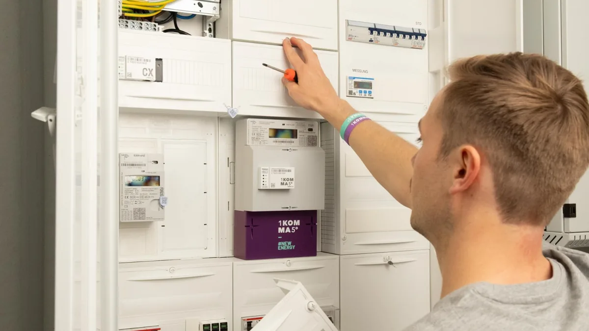 Junger Monteur in grauem T-Shirt öffnet einen Zählerschrank mit digitalen Stromzählern und einem Smart-Meter-Gateway