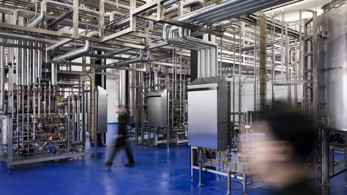 Zwei Mitarbeitende von Solar Foods in der Factory 01 in Vantaa – Blick auf die Produktionshalle mit Bioreaktoren, Rohrleitungen und blauem Hallenboden