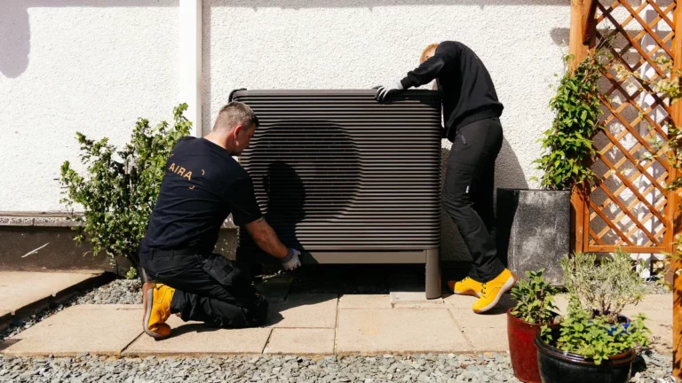 Zwei Aira-Monteure installieren eine Luft-Wasser-Wärmepumpe an der Außenwand eines Wohnhauses